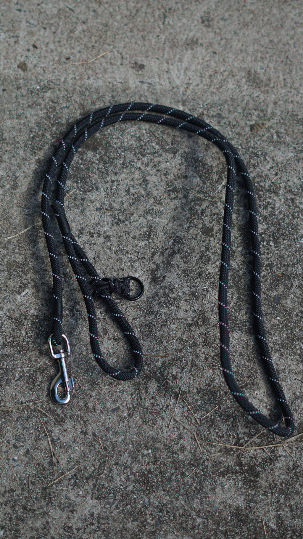 Black dog leash with metal clip on a concrete surface