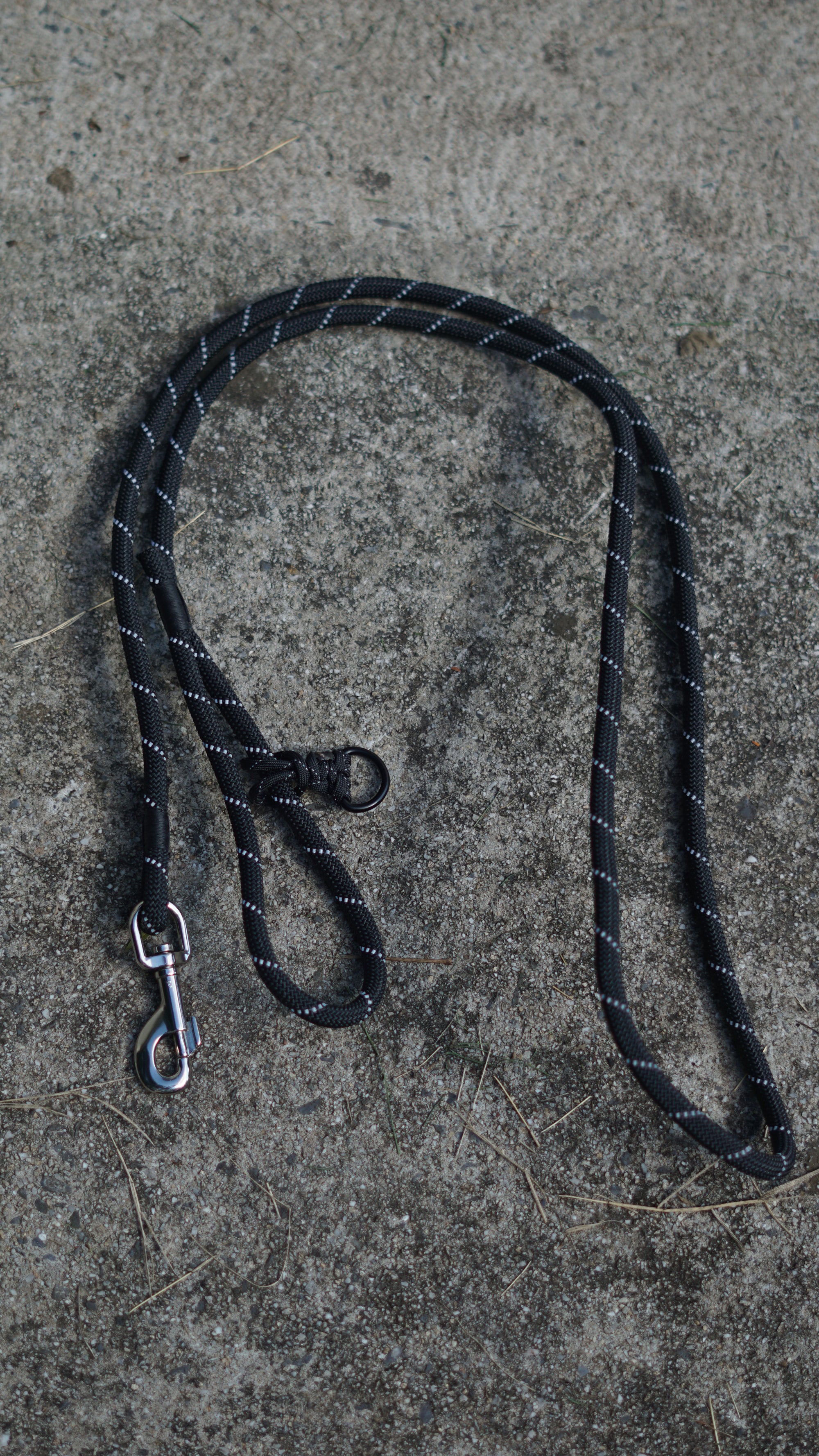 Black dog leash with metal clip on a concrete surface